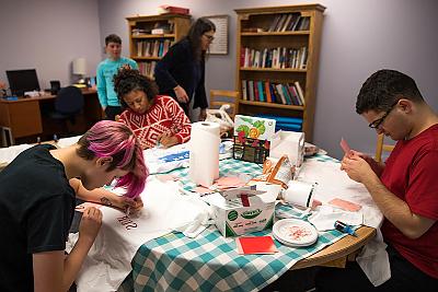 一群学生围坐在妇女与性别中心的一张桌子旁. 他们正在制作印有“性骚扰意识日”口号的t恤. 